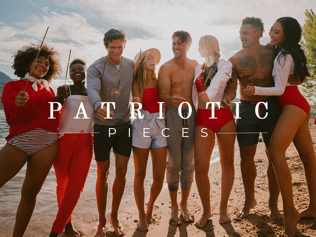Group of people pose in patriotic red, white, and blue outfits on a sunny beach while holding sparklers
