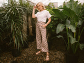 Front view of Audrey Wide Leg Pants showcasing a pink-and-cream checkered wide-leg fit on a model in a lush indoor garden