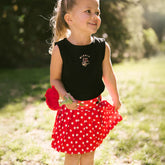 Young girl standing in a park wearing the perfect kids Disney outfit—red polka dot Minnie skirt for kids and black Minnie shirt for kids.