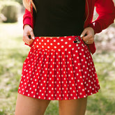 Close up of woman wearing red polka dot Minnie Mouse tennis skirt on a blurred greenery background.