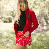 Woman standing in a garden wearing a Disney tennis skirt in red polka dot print with Minnie Mouse tank and red bomber jacket.