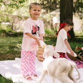 Two young girls feeding baby lambs and wearing cute Disney outfits for kids—the perfect pink Minnie Mouse tee for kids.