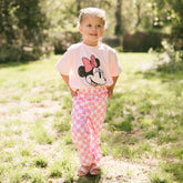 Child wearing a kid's Minnie Mouse shirt and pink checkered kid's Disney pants standing in a grassy outdoor area.