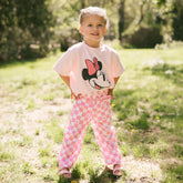 Child standing in a garden wearing pink checkered Disney pants for kids with a pink Minnie Mouse shirt for kids.