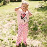 Child wearing a cute Disneyland outfit for kids with a pink Minnie shirt and pink check Minnie pants on a blurred grassy background