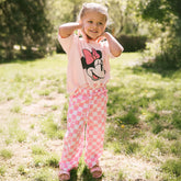 Young girl standing outdoors wearing an easy Disneyland outfit for kids—pink Disney pants for girls and a Minnie Mouse shirt for kids.