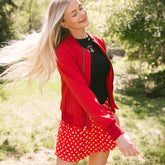 Woman twirling in a park wearing a subtle Disney outfit—a red bomber jacket with Mickey Mouse on it, a Minnie tank top and Minnie tennis skirt.