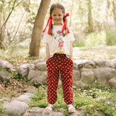 Young girl in a forest wearing a white Disney shirt for kids with red polka dot Disney pants for kids with hidden Minnie Mouse icons.