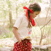 Young girl with red bows in her hair wearing a Mickey t shirt for kids and red polka dot kids pants for Disneyland.