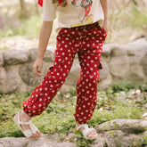 Child wearing kid's Disney pants in Minnie Mouse print red polka dots with cargo pockets on a blurred garden background