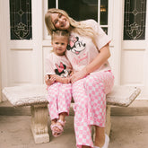 Mom and daughter sitting on a bench wearing matching Disneyland outfits for families—pink Minnie Mouse shirts and Minnie Mouse pants.