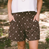 Close up of cute women's bermuda shorts for Disney in brown Minnie Mouse print on a blurred garden background.
