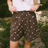 Close up of woman wearing subtle Disney outfit—brown Disney shorts for women with Minnie Mouse print on a blurred greenery background.