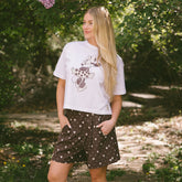 Woman standing in a garden wearing the perfect Disneyland outfit—white stylish Minnie Mouse t-shirt and comfy Disney shorts.