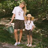 Woman and child standing in a garden wearing matching Disneyland outfits—kids Minnie tee with kids Disney shorts in brown.