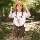 Child wearing a cute kids Minnie t shirt with subtle Disney shorts in Minnie Mouse print on a blurred greenery background.