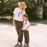 Woman and child wearing matching Disney outfits—neutral Minnie Mouse t-shirts and women's Disney pants in Minnie Mouse print.