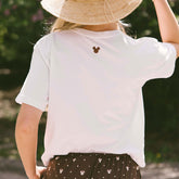 Close up back view of woman wearing a Disney t-shirt with Mickey mouse embroidery on the neck with a blurred background.