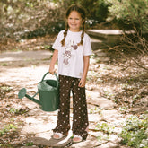Child wearing a cute kid's Disney outfit—kid's Disney pants in Minnie Mouse print holding a watering can in a garden.