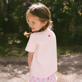 Young girl wearing a light pink, kid's Cinderella shirt with a pink crown design outdoors.