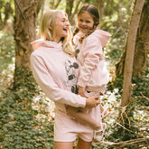 Woman holding a child in the forest while wearing matching outfits for Disneyland in light pink.