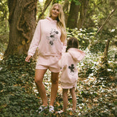 Two people wearing matching pink outfits with Minnie Mouse design in a forest setting.