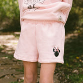 Close up of child wearing little girls Minnie Mouse shorts on a blurred greenery background.