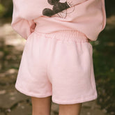 Close up back view of girl wearing pink Minnie Mouse shorts on a blurred green background.