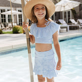 Young girl in a blue striped kids two piece swimsuit with little girls swim skirt and sun hat by a pool