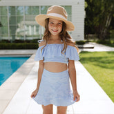 Young girl in a blue striped two piece swimsuit and sun hat standing by a pool.