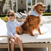 Child and dog sitting on a lounge chair outdoors—child is wearing a blue stripe rash guard swimsuit for kids.