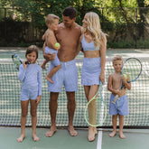 Family of five on a tennis court wearing matching family swimsuits with tennis rackets and balls.