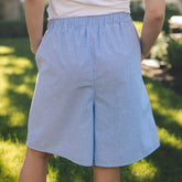 A person outdoors wearing light blue shorts with an elastic waistband and side pockets, standing on a grassy lawn.