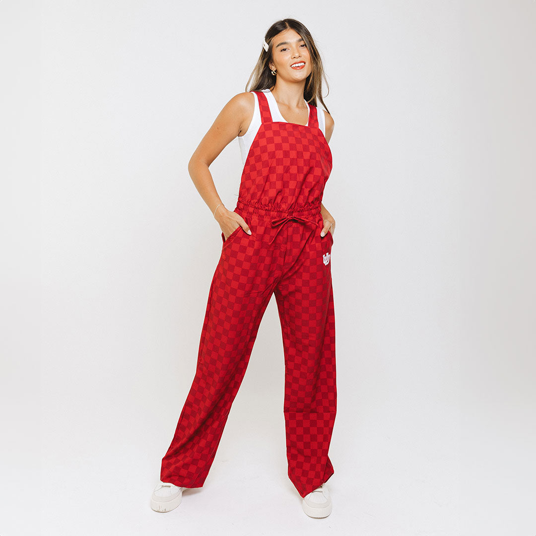 A woman standing, wearing red checkerboard print overall trousers with pockets and a cinch waistband.