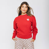 A woman wearing a red crewneck sweater with an embroidered Utah patch on the left chest area, paired with checkered pants.