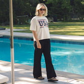 Woman wearing a cute women's 4th of July shirt with USA 1776 screen printing and black trousers walking next to a pool