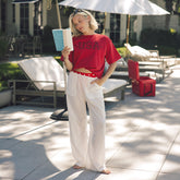 Woman in red USA t-shirt and white pants standing outdoors with a book, wearing sunglasses.