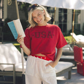 Woman in a red USA women's t-shirt holding a book outdoors.