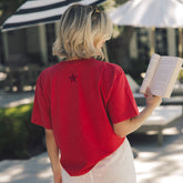 Woman wearing a red t-shirt with a star on the back, holding a book outdoors.