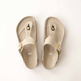 Pair of beige sandals—Birkenstock Gizeh Big Buckle—with gold buckles on a white background