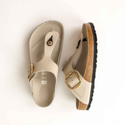 Pair of beige sandals with gold buckles on a white background. Birkenstock Gizeh Big Buckle
