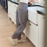 Woman wearing cute women's balloon pants in navy gingham standing against a sink washing her hands.