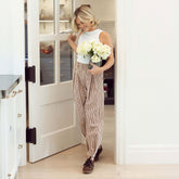Woman wearing a white tank top and brown gingham, flattering balloon pants holding a vase of flowers