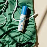 Angled view of Vacation Super Spritz SPF 50 Face Mist showcasing its blue cap on green fabric