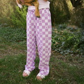 Close up of young child wearing girls Minnie Mouse pants in purple check print standing outside in a garden