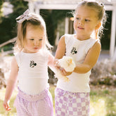 Two young girls standing together holding a baby chick and wearing matching Disney tank tops—Minnie Mouse tank tops for kids.