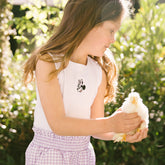 Young girl holding a small chicken and wearing a kid's Minnie Mouse tank top outdoors with greenery in the background