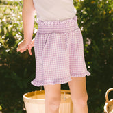 Close up of young child wearing kid's gingham shorts in purple on a blurred garden background
