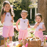 Three young girls in matching Disneyland outfits featuring Daisy Duck tank tops and pink gingham kids shorts standing outdoors with a basket and flowers.