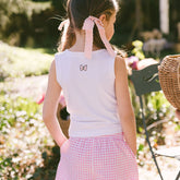 Back view of child wearing a white tank top for Disneyland with a pink bow on the back on a blurred garden background